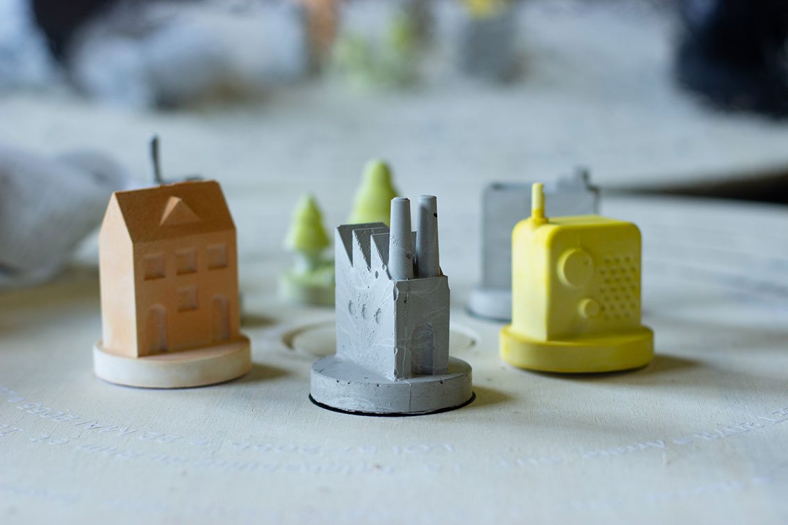 Petits bâtiments en béton et résine teintés : une maison, une usine et une radio, issus de Fictions urbaines